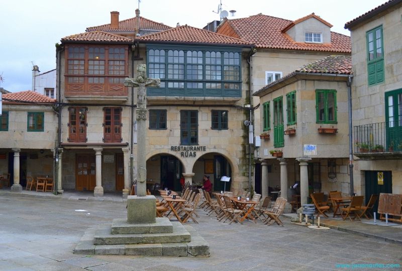 Vista de la Praza da Leña con el cruceiro del siglo XVIII en el centro, rodeado de edificios y soportales históricos.