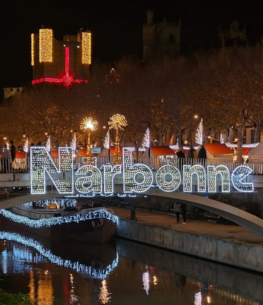 Iluminación navideña con letrero luminoso de Narbonne reflejado en el Canal de la Robine