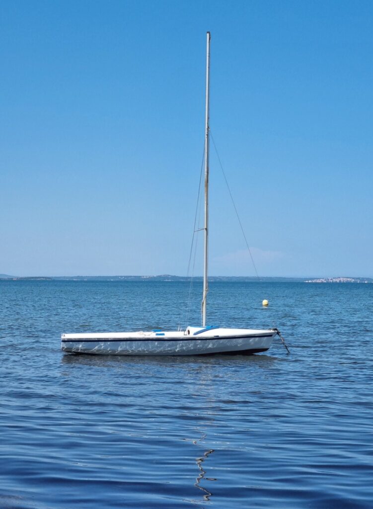 Velero en las aguas tranquilas del lago de Leucate bajo un cielo azul