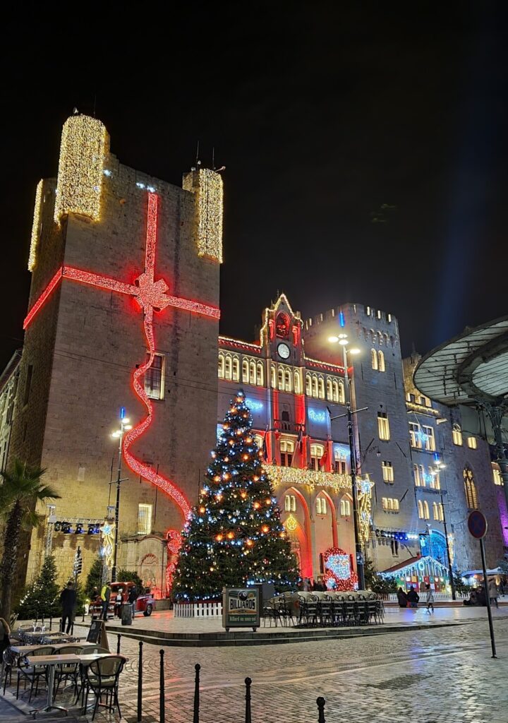 Plaza del Ayuntamiento de Narbonne iluminada en Navidad con torre decorada y árbol de Navidad