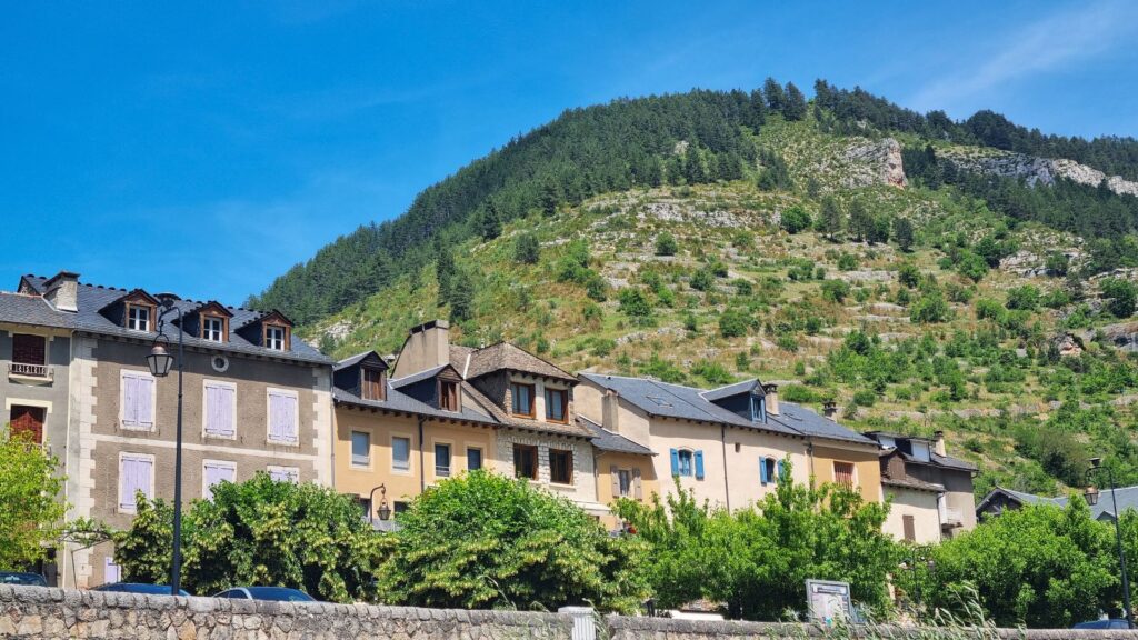 Hilera de casas de piedra con postigos de colores bajo la ladera boscosa en Sainte-Énimie, Lozère